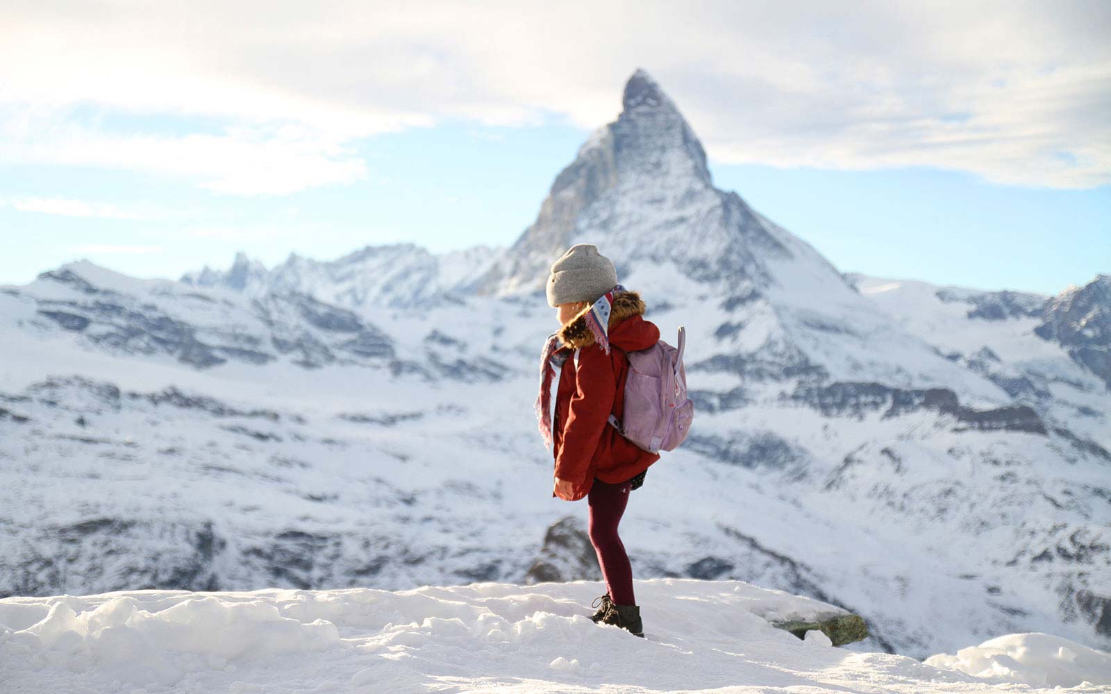 Child standing in the snow with mountains behind